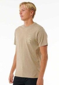T-shirt in cotone beige con collo a giro, maniche corte e un piccolo logo bianco stampato sul petto. Texture liscia e vestibilità rilassata.