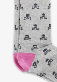 Calcetines grises con un patrón de calavera y huesos cruzados, con acentos rosas en la puntera y el talón. Fabricados con un material de punto suave.