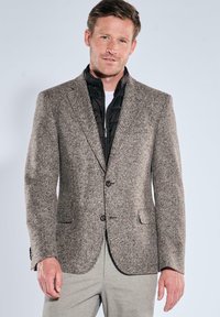 Brauner Blazer mit Hahnentrittmuster, mit Kerb-Revers, zwei Knöpfen und Vordertaschen, kombiniert mit einer schwarzen gesteppte Jacke und hellgrauen Hosen.