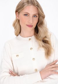 White knit cardigan with horizontal ribbed texture, golden buttons, and a pocket detail. Features a round neck and long sleeves.