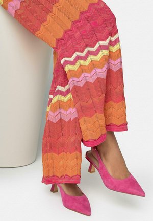 Überkreuzte Beine mit bunten Zickzack-musterigen Hosen in Pink, Orange, Gelb und Weiß, kombiniert mit pinkfarbenen Wildleder-Slingback-Absatzschuhen mit spitzer Spitze.