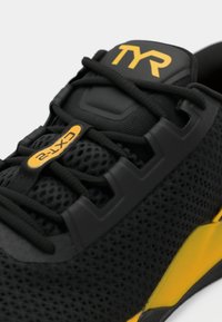 Czarne buty sportowe z siateczkową cholewką, z żółtymi akcentami i logo TYR. Posiadają detal teksturowany i bezpieczny system sznurowania.