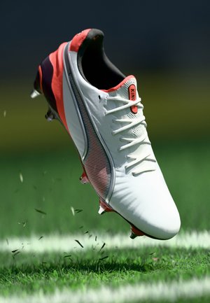 White football boot with red accents, textured surface, and mesh details. Cleats on sole, raised off a grassy field.