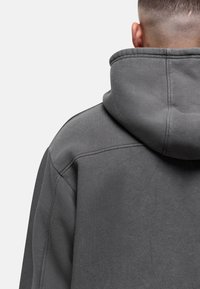 Felpa grigia con cappuccio in morbido tessuto, cuciture sulle spalle e design con colletto alto. Si distingue per linee pulite e uno stile minimalista.
