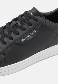 Black leather sneaker with sturdy lace-up design, contrasting white sole, and a silver logo detail on the side. Smooth texture.