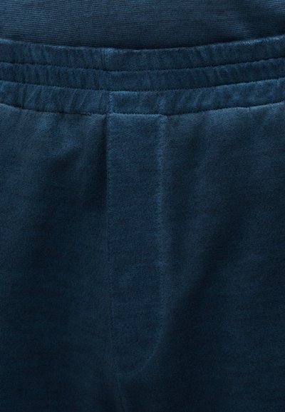 Ύφασμα σε ναυτικό μπλε χρώμα, με ομαλή υφή, άνετη ελαστική μέση και ραμμένες λεπτομέρειες κατά μήκος των πλευρών.