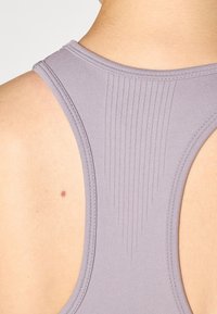 Débardeur de sport violet avec un dos en scoop et une texture côtelée verticale le long de la colonne vertébrale. Tissu léger avec des coutures contrastées.