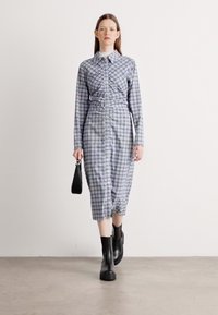 Abito camicia a quadri blu e bianchi con vita aderente, chiusura a bottoni, maniche lunghe e lunghezza fino al polpaccio. Abbina a stivaletti neri alla caviglia.