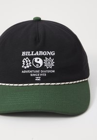 Black fabric cap with a green brim. Features white embroidered logos: trees, yin-yang, sun, and text "BILLABONG ADVENTURE DIVISION SINCE 1973."