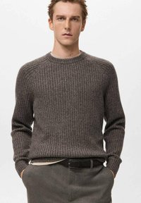 Szary sweter z prążkowanego dzianiny, z okrągłym dekoltem, długimi rękawami i teksturowaną powierzchnią. W połączeniu z ciemnymi spodniami i czarnym paskiem.