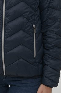 Doudoune marine avec un matelassage en chevrons, dotée de deux poches zippées et d'une finition brillante et légère. Ourlet réglable pour un ajustement optimal.