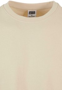Licht beige t-shirt met korte mouwen van zachte katoen. Heeft een ronde halslijn en een label dat binnenin de kraag is genaaid. Glad textuur.