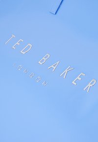 Modrá syntetická taška s embosovaným logom "TED BAKER LONDON" v striebre. Hladký povrch s plochými uchami na nosenie.