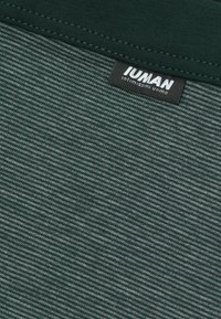 Grönrandig tyg med en mjuk textur. Fäst etikett med "IUMAN"-varumärke. Ränderna växlar mellan mörk och ljus grön.