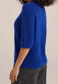 Maglione lavorato a maglia di un blu vivace, con maniche corte e una finitura morbida e testurizzata. Il design è aderente in vita.