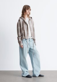 Cropped, plaid brown shirt with a hood, paired with loose light blue jeans and black slip-on shoes. White belt adds contrast.