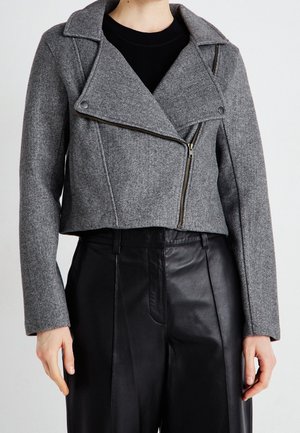 Person wearing a cropped gray wool jacket with an asymmetrical zipper and black high-waist leather pants against a plain background.