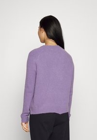 Pull tricoté violet, col rond, manches longues, ourlet et poignets côtelés, avec un petit logo au niveau de la nuque à l'arrière. Texture lisse.