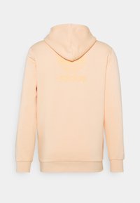 Persikofärgad hoodie med en känguruficka, justerbar dragsko på huvan och präglad Adidas-logotyp på baksidan. Mjuk textur, standard passform.