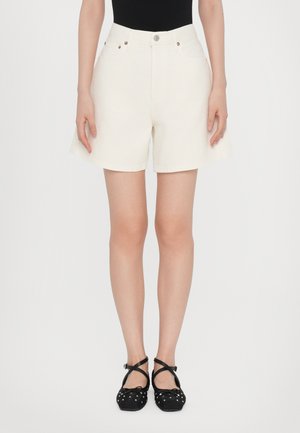 Kremfargede denimshorts med løs passform, høyt liv, frontlommer og lukkes med metallknapp. Kombinert med svarte, flate sandaler med stropper.