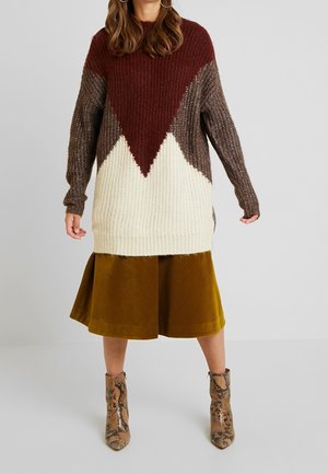 Pull en tricot avec un design de blocs de couleur bordeaux, marron et crème, associé à une jupe moutarde et des bottines à imprimé serpent marron.