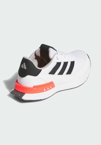 White athletic shoe with black accents and three stripes, featuring a textured upper, padded collar, and a bright orange heel clip.