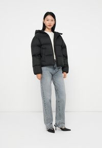 Svart vadderad jacka med huva, framdragkedja, kort design; använd med ljusblå jeans och svarta spetsiga klackar. Slät textur, minimalistisk stil.