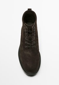 Stivale alla caviglia in suede marrone con punta rotonda, sei occhielli, lacci neri e suola in gomma. Presenta un design cucito lungo il bordo della suola.