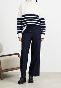 Chunky stickad tröja i kräm med marinblå horisontella ränder, högkragningsdesign. Kombinerad med mörk marinblå vida byxor och svarta kraftiga stövlar.