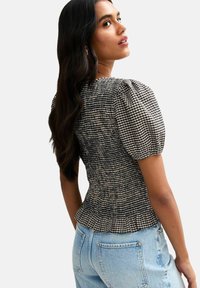 Black and white checkered fitted blouse with puff sleeves and smocked texture, paired with light blue high-waisted jeans.