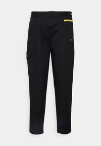 Pantaloni cargo neri con una vestibilità slim, dotati di tasche laterali e posteriori, un accento giallo sul retro e un piccolo logo bianco vicino alla tasca.