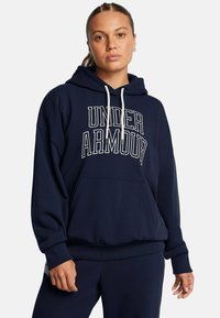 Navyblaue Kapuzenjacke mit "UNDER ARMOUR" in weißem Text, lockere Passform, Kordelzug-Haube, Fronttasche, gerippte Bündchen und Saum. Weicher Stoff.