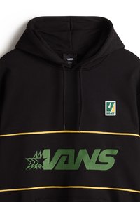 Sweat à capuche Vans noir avec logo Vans vert et motif étoile sur la poitrine, petite étiquette rectangulaire Vans au-dessus, et rayures horizontales jaunes.