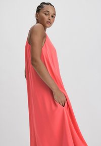 Hihaton koralli mekko, joka on valmistettu pehmeästä kankaasta ja jossa on rento istuvuus sekä sivutaskut. Muotoilu tarjoaa sujuvan ja virtaavan siluetin.