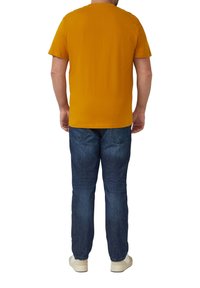 Mustard yellow short-sleeve t-shirt with a crew neck, paired with dark blue jeans and light-colored shoes, viewed from the back.