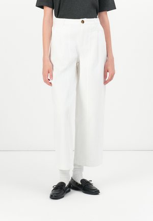 Witte wijde broek met een knoopsluiting, met een gladde stofstructuur. Gecombineerd met zwarte instappers en witte sokken.