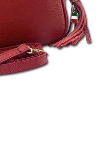 Eine stilvolle rote Handtasche aus Leder mit einem langen Tragegurt und einer dekorativen Quaste, die mit einem kleinen Charm der italienischen Flagge verziert ist.