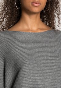 Pull gris à côtes avec un large col, présentant un motif de tricot texturé. Le tissu semble doux et légèrement extensible.