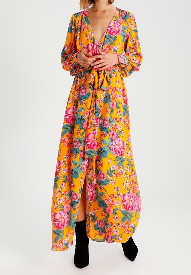 Maxiklänning i starkt gult med blommönster som har rosa och gröna accenter. Långa ärmar, djup V-ringning och midjebandsdetalj.