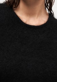 Μαύρο πουλόβε ρ από μαλλί με απαλό, υφασμάτινο φινίρισμα. Διαθέτει φαρδιά, στρογγυλεμένη λαιμόκοψη και στενή εφαρμογή, κατάλληλο για στρώσεις.