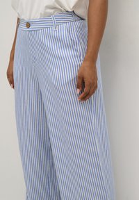 Pantaloni leggeri a gamba larga con strisce verticali blu e bianche. Presentano una chiusura con bottone anteriore, tasche laterali e una vestibilità rilassata.
