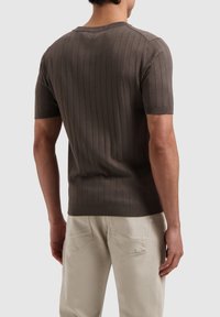 Bruine ribgebreide trui met korte mouwen en een ronde hals, met een gladde textuur, gedragen met lichtkleurige broek, weergave van achter.
