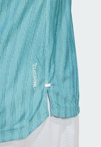 Camisa atlética azul claro con tejido texturizado y patrones verticales, aberturas laterales y la marca "Climacool+" cerca del dobladillo.