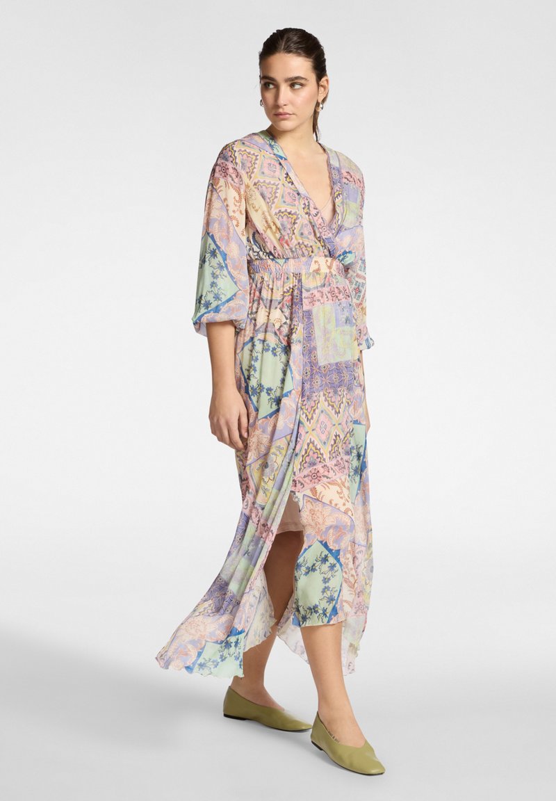 Vestido ligero con estampado en colores pastel, escote en V profundo, mangas anchas, cintura con cordón y dobladillo fluido. Combinado con zapatos verdes.