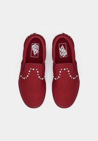 Røde slip-on Vans-sko med en glatt tekstiloverdel, rund tå og hvit nagledesign over fronten. Gummisåler.