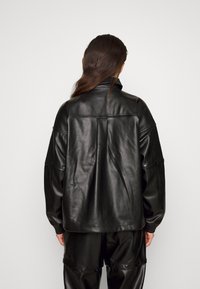 Svart läderjacka med avslappnad passform, som har hög krage, sänkt axlar och synlig sömnad på baksidan. Slät textur.