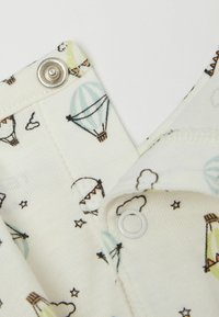 Bílá látka s barevným vzorem horkovzdušných balónů a mraků. Obsahuje stříbrné patentky a kontrastní krémové lemování.