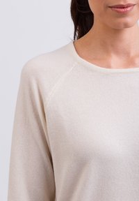 Hellbeiger Pullover mitweichem Textil, weitem Ausschnitt und Raglanärmeln. Der Stoff hat eine feine Strickoberfläche und bietet einen lässigen Stil.
