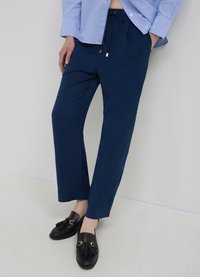 Pantalon bleu marine fuselé en tissu léger avec une ceinture élastique à cordon ; associé à des mocassins noirs ornés de glands décoratifs.