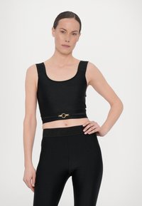 Top sportivo nero tagliato con spalline larghe, dotato di un accento circolare dorato in vita. Tessuto liscio e elasticizzato con un design aderente.